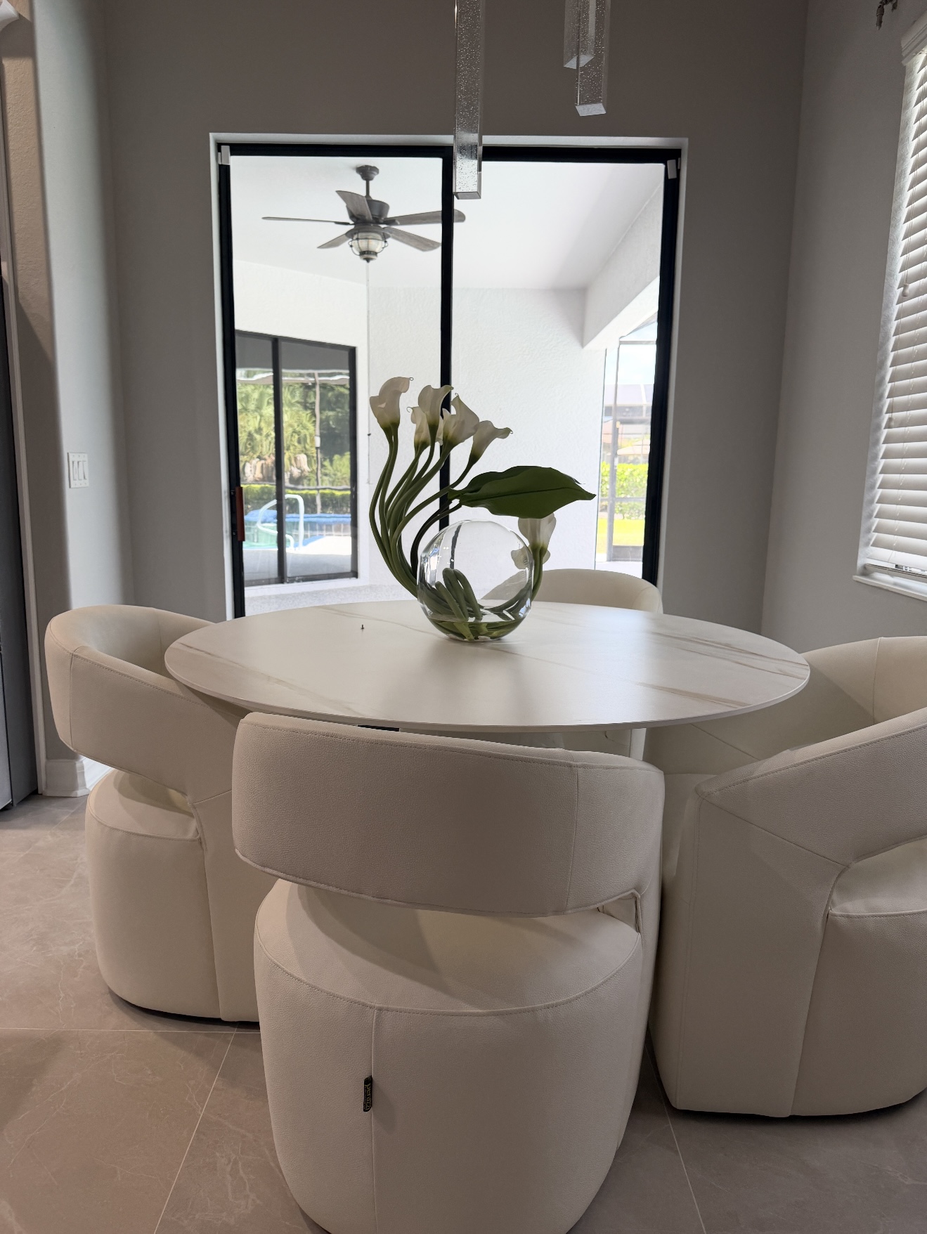 A clean round dining table with white chairs and a vase of flowers